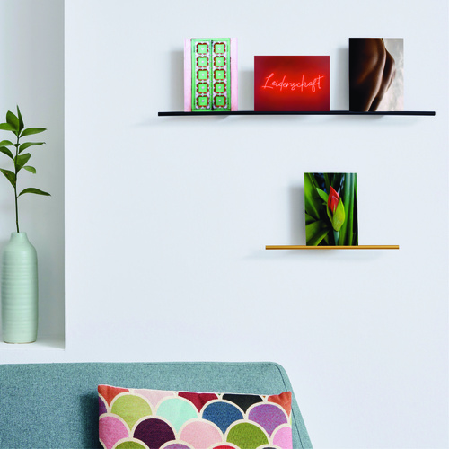 Zwei Cartes-Bilderleisten, in Schwarz und in Gold, horizontal vor einer weißen Wand, bestückt mit verschiedenen Motiv-Postkarten: Blume, Muster, Körperausschnitt, Schriftzug